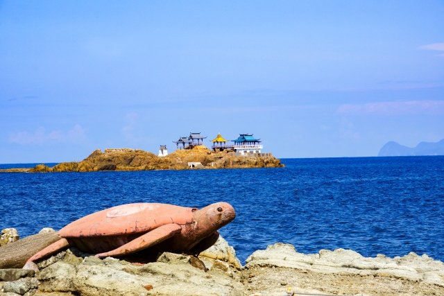 A turtle statue overlooking the sea with a scenic offshore shrine near Kinosaki Onsen, highlighting the region’s coastal charm.