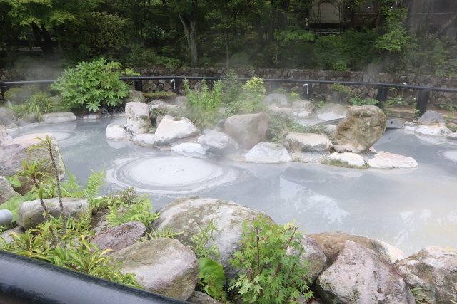 Beppu Onsen famous Shiraike Jigoku, a steaming white pond surrounded by rocks and greenery.