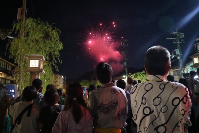 Crowds in yukata watching fireworks light up the night sky during a summer festival in Kinosaki Onsen.