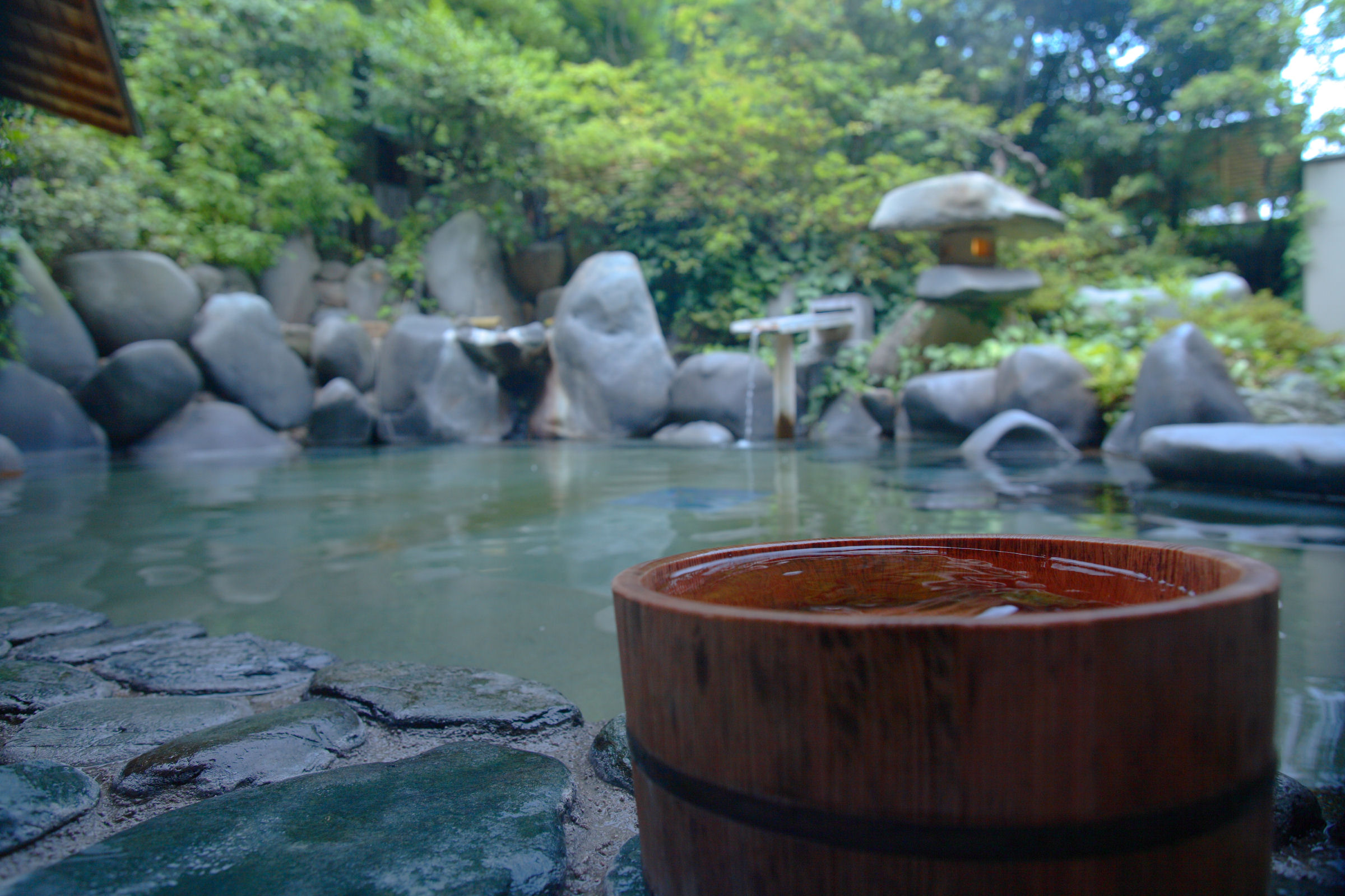 Tamatsukuri Onsen Izumo serene open-air hot spring with traditional wooden bucket and natural rock setting.
