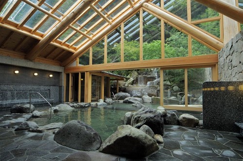Spacious indoor hot spring bath with a glass roof and natural rock setting in Kinosaki Onsen, blending relaxation with scenic beauty.