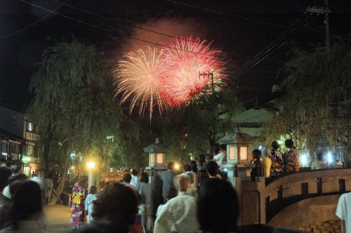 Crowds gathered on a bridge to watch fireworks during a summer evening in Kinosaki Onsen, celebrating the festive atmosphere.