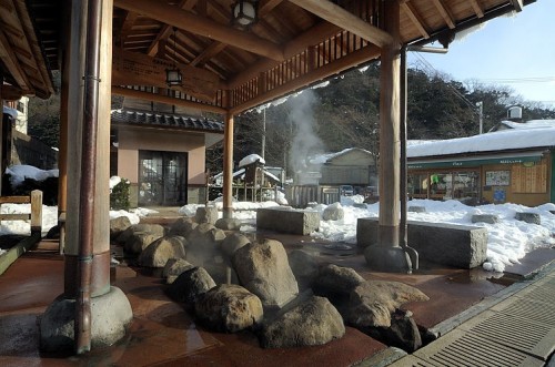 Open-air footbath with natural hot spring steam rising amid a snowy setting near Dogo Onsen.
