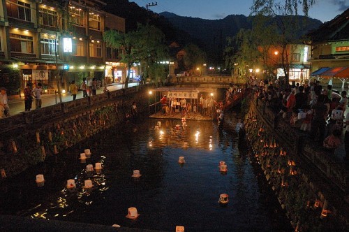 Lanterns floating on the river during a summer festival night in Kinosaki Onsen, with crowds enjoying the lively celebration.