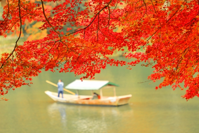 Traditional boat on the Oi River framed by vibrant autumn leaves in Arashiyama Kyoto.