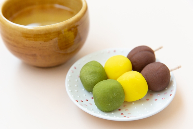 Colorful skewered dango sweets—green, yellow, and brown—served with Japanese tea. A specialty treat found in the Dogo Onsen area.