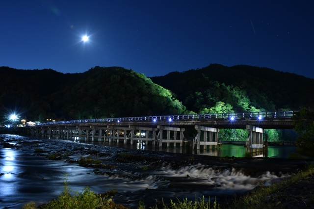 Togetsukyo Bridge illuminated under the moonlight in Arashiyama Kyoto, with the Hozugawa River gently flowing beneath.