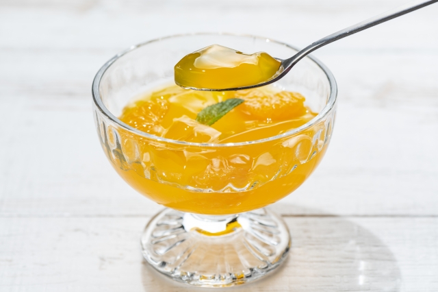 A close-up of a glass dessert cup filled with citrus jelly, with a spoon lifting a translucent piece of jelly above the cup.