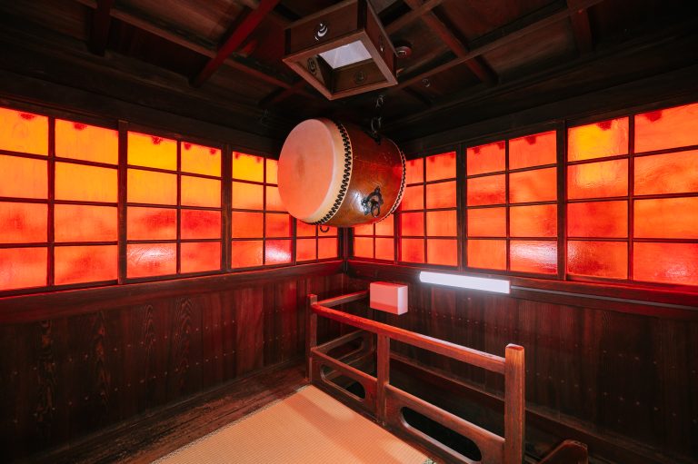 Traditional taiko drum in the red-lit drum tower of Dogo Onsen, used for marking time and welcoming guests.