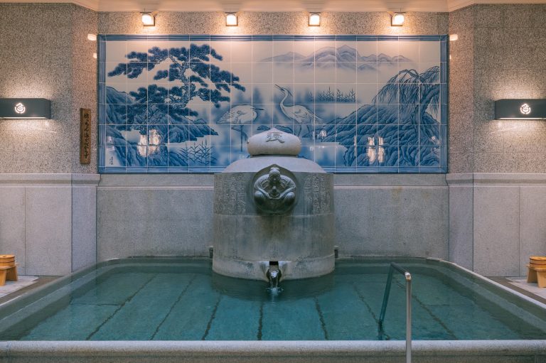 Indoor bath at Dogo Onsen with a decorative blue tile mural and symbolic fountain, reflecting the rich artistic heritage of Japan’s oldest hot spring.
