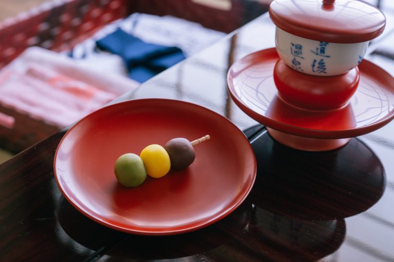 Traditional sweets and tea set served at Dogo Onsen, featuring a colorful dango skewer and a cup labeled with “Dogo Onsen” in kanji.