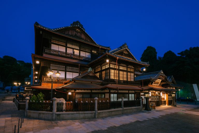 Dogo Onsen Honkan beautifully illuminated at night, showcasing the elegance of Japan’s oldest wooden bathhouse.