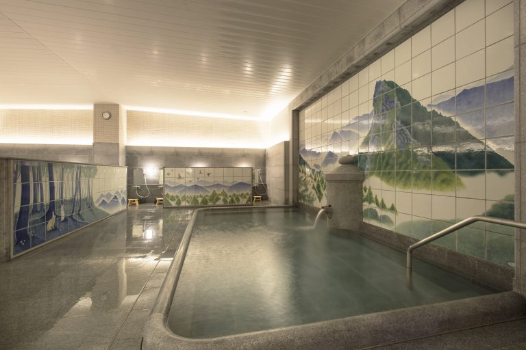 Indoor bath of Dogo Onsen with scenic tile art of mountains and forests, offering a serene hot spring experience.