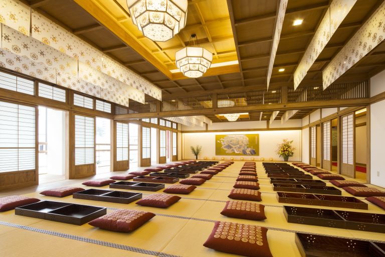 Spacious tatami room at Dogo Onsen with red floor cushions and elegant wooden architecture, used for traditional gatherings or rest.