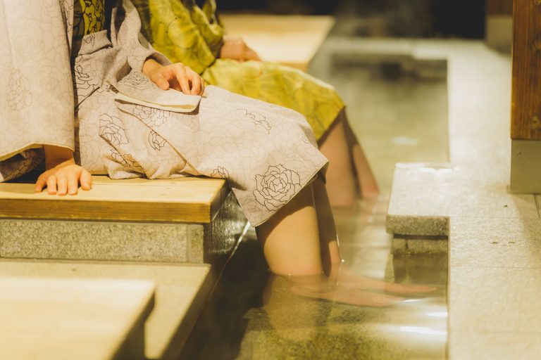 Visitors in yukata soaking their feet in a relaxing footbath at Dogo Onsen, enjoying the warmth and tranquility of the hot spring experience.